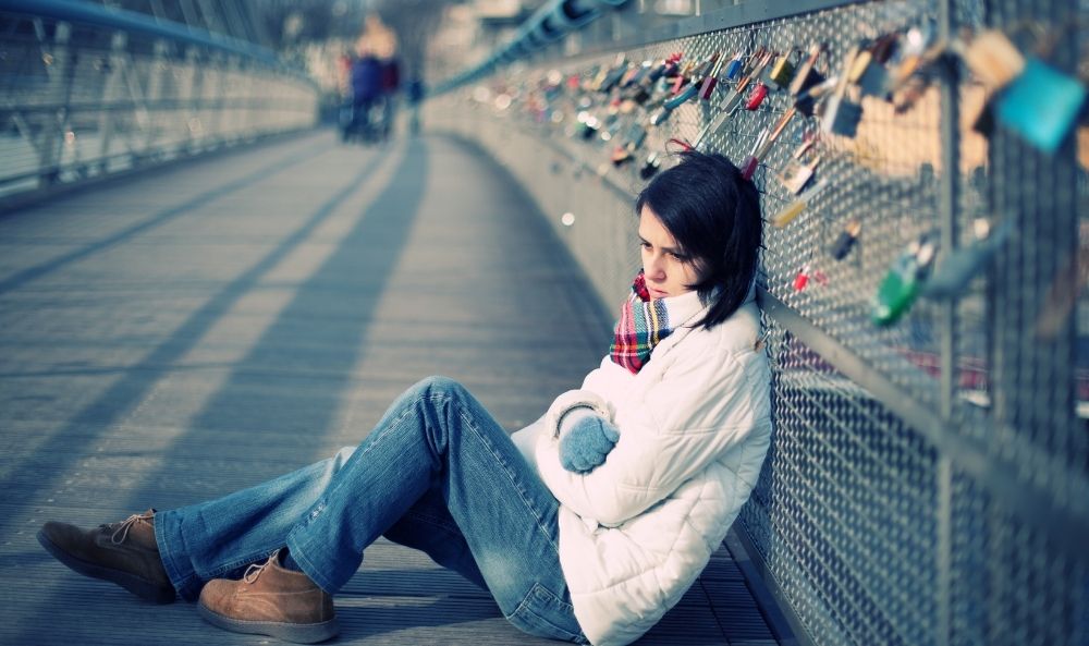 Mujer sentada sola en un puente sufriendo los efectos del ghosting